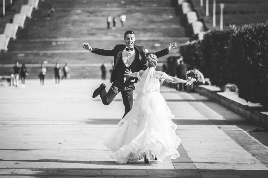 Moment surprins de fotograf la sedinta foto de nunta in Bucuresti: mirele sare de bucurie in fata miresei, in parc.