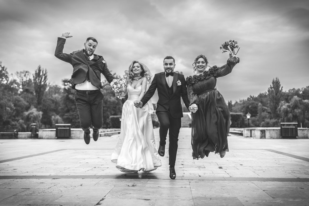Mirii cu nasii sunt surprinsi de fotograf sarind, in parcul Carol din Bucuresti, la sedinta foto de nunta.
