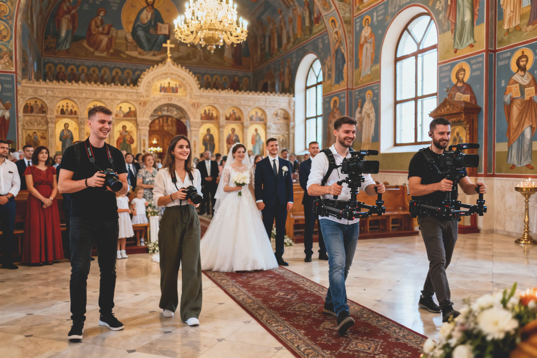 Echipa foto video, fotografi si videografi de nunta, lucrand sincronizat in interiorul unei biserici ortodoxe in timpul cununiei.