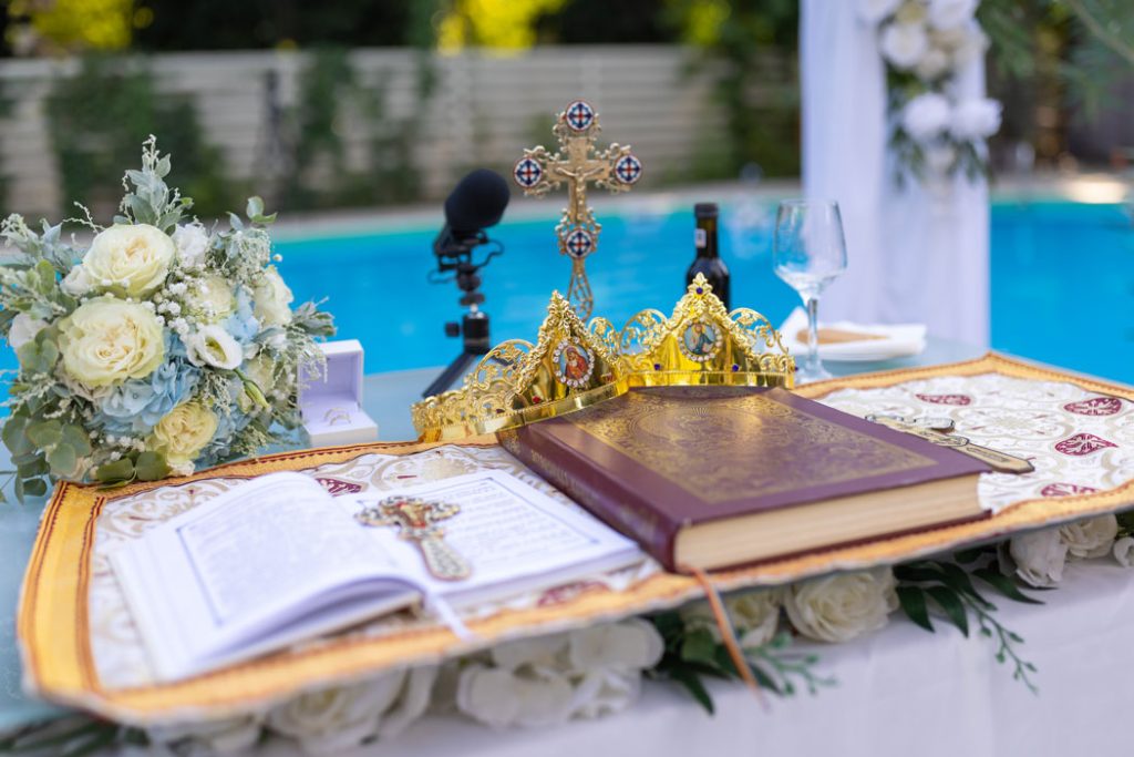 Fotograful de nunta surprinde Evanghelia, Cununiile, Crucea sfanta, aranjate pe o masa improvizata langa piscina, pentru Taina Cununiei