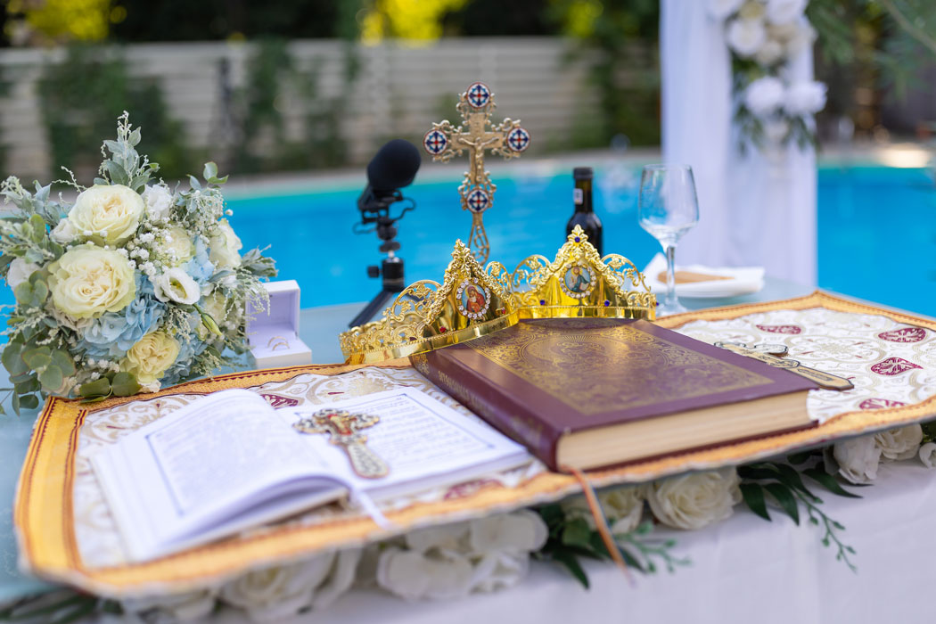 Fotograful de nunta surprinde Evanghelia, Cununiile, Crucea sfanta, aranjate pe o masa improvizata langa piscina, pentru Taina Cununiei