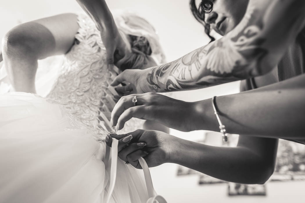 Moment surprins de fotograf nunta in Bucuresti: domnisoarele de onoare inchid rochia miresei.