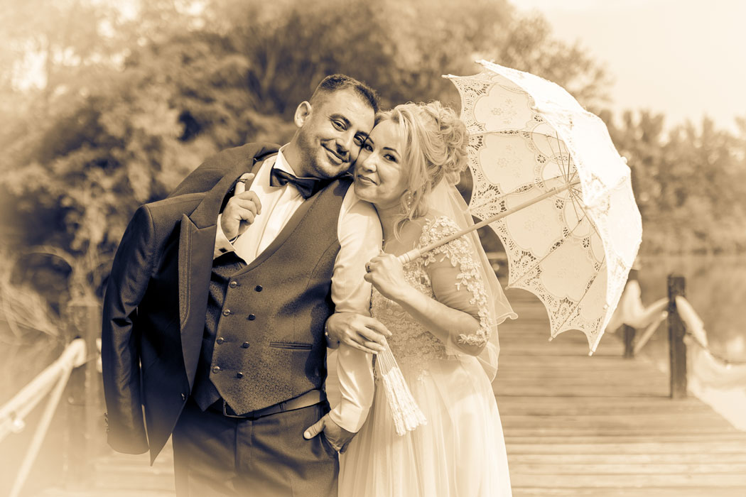 Fotografie vintage, mireasa cu umbrela tine mirele de brat pe malul unui lac, surprinsi de fotograf nunta Bucuresti