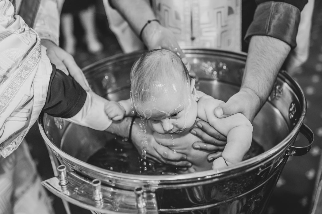 La botez, bebelusul este surprins de fotograf in cadelnita, cu apa botezului pe cap
